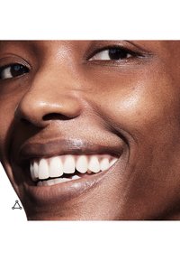 Primo piano di un volto sorridente con pelle liscia e scura, denti bianchi e lineamenti ben definiti. La luce si riflette sulla texture della pelle.