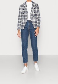 Kaksirivinen ruudullinen bleiseri laivastonsinisen ja valkoisen sävyissä, yhdistetty korkeavyötäröisiin sinisiin farkkuihin ja valkoisiin tennareihin. Sileä tekstuuri, räätälöity istuvuus.