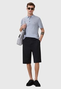 Ljust blå pikétröja med kort ärm och tre knappar, kombinerad med svarta knälånga shorts och svarta skor. Inkluderar en grå toteväska.