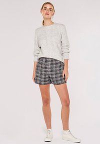 Grå stickad tröja med ett strukturerat mönster som är kombinerad med svartvit rutiga shorts. Modellen bär vita hög-låga sneakers.