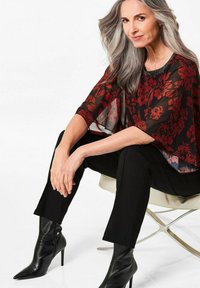 Top trasparente nero con stampa floreale e scollatura rotonda, abbinato a pantaloni neri sartoriali e stivali neri con tacco a spillo.