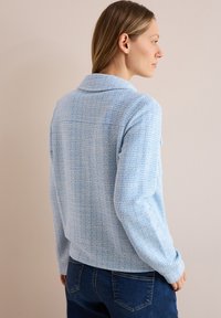 Lichtblauwe tweedjas met een textuurfinish, enkelvoudig ontwerp, geknipte kraag en lange mouwen. Gecombineerd met donkerdenim jeans.