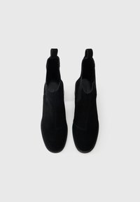 Μαύρες σουέτ μπότες αστραγάλου με ελαστικά πλαϊνά πάνελ και θηλιές για εύκολη χρήση. Απαλή επιφάνεια με στρογγυλή μύτη και επίπεδες καουτσούκ σόλες.