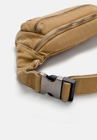 Fanny pack in tela color sabbia con due scomparti con zip e una tracolla piatta con fibbia. Tessuto testurizzato con dettagli cuciti.