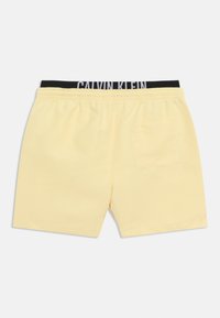 Ανοιχτό κίτρινο ανδρικό σορτς με ελαστική μέση και εμφανές μαύρο λογότυπο Calvin Klein, με πίσω τσέπη στη δεξιά πλευρά.
