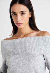 Gray off-shoulder sweater made of soft knit fabric, featuring a wide ribbed neckline and a textured finish. Simple design with no patterns.