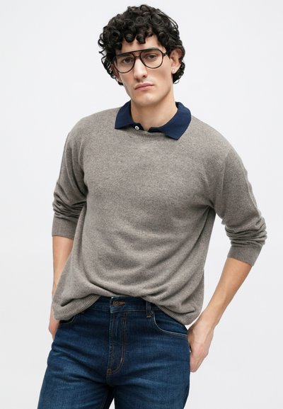 Hall halliaga kampsun tumesinise kraega, millel on soonikkoes mansetid ja lõdvestunud lõige, sobitatud tumedate siniste teksadega.