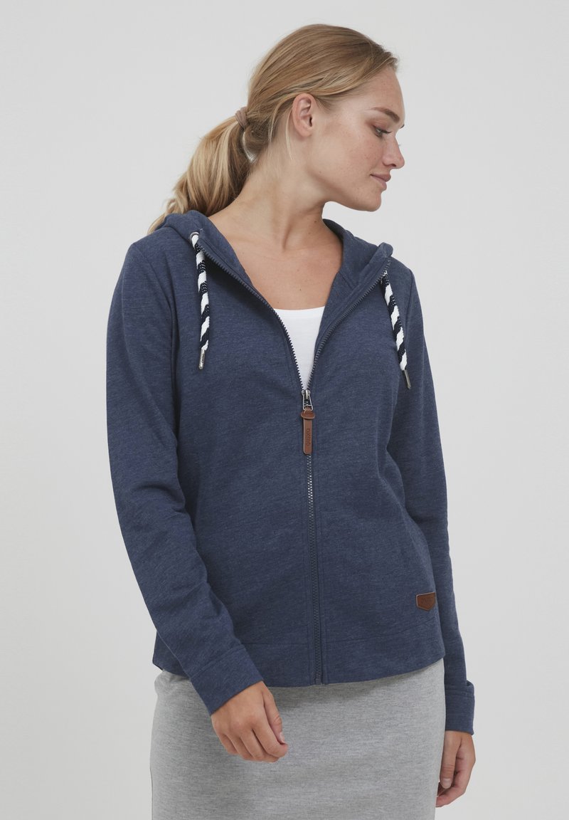 Mornarska zip-up kapuca, izdelana iz mehke tkanine, z naramnicami v črtastem vzorcu, z zadrgo in majhnim rjavim usnjenim logotipom.