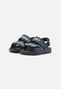 Infradito blu navy con due larghe cinghie che presentano scritte bianche. Il materiale sembra gommoso e le suole sono piatte con una superficie testurizzata.