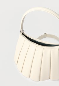 Κρεμ τσάντα με πτυχώσεις, με κοντό λουρί και ασημένιο φερμουάρ, παρουσιάζεται πάνω σε απλό φωτεινό φόντο.