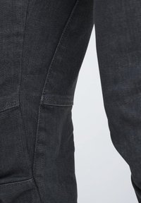Dunkelblaue Denim-Jeans mit glatter Textur, tailliertem Schnitt und dezenten Steppdetails. Die Taschen befinden sich an den Seitennaht.