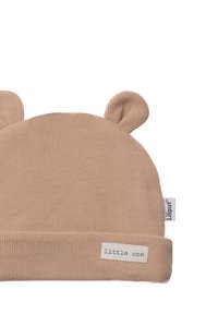 Beige Strickmütze mit Bärenohren, umgeschlagenem Design, weichem Material und einem Etikett mit der Aufschrift "little one" an der Seite.