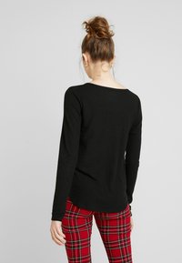 Schwarzes Langarmshirt aus geripptem Stoff mit weitem Ausschnitt, kombiniert mit roten Karohosen mit schwarzen und grünen Akzenten.
