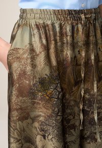 Braun und grün gemusterte Hose mit elastischem Bund, seitlichen Taschen und einem Kordelzug, aus einem strukturierten Stoff mit Naturdesign.