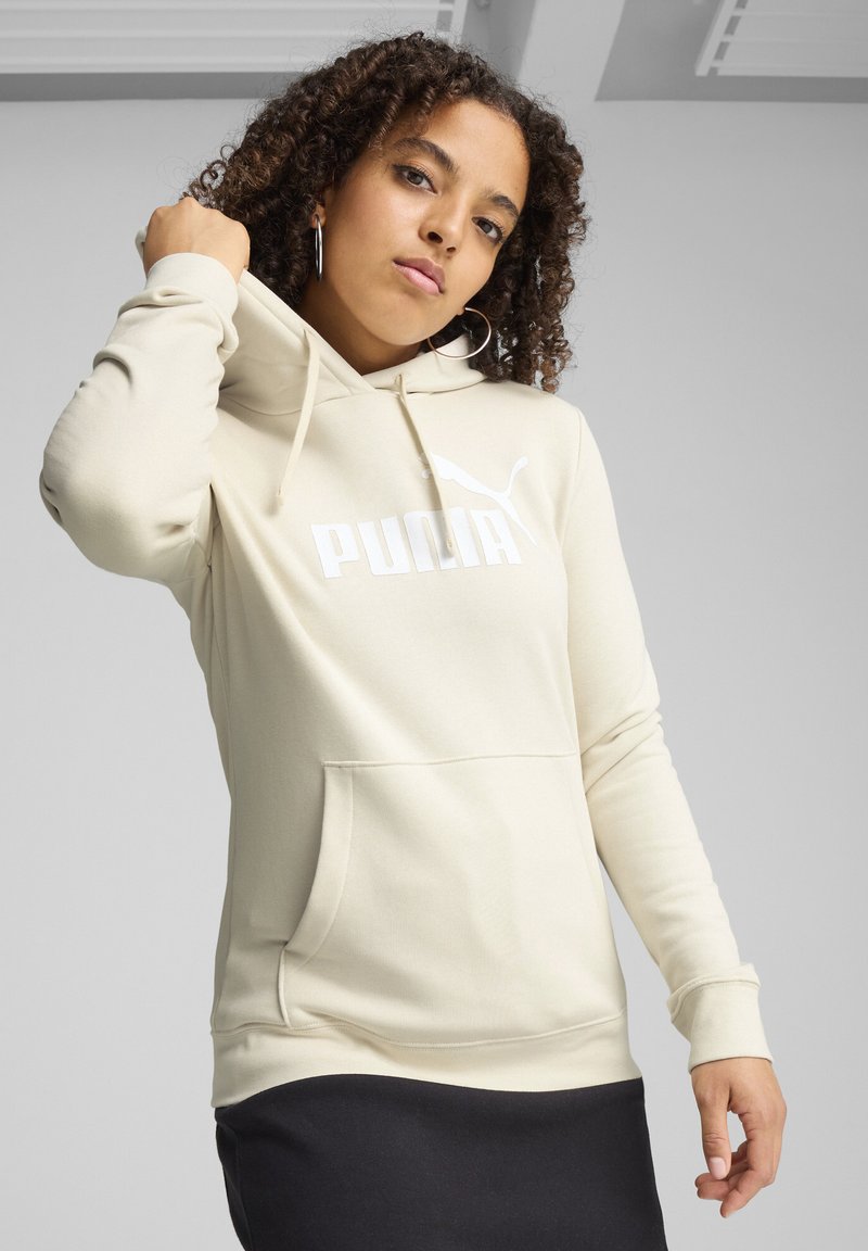 Sudadera con capucha beige con un bolsillo frontal, que presenta un logo blanco de "PUMA". Tejido suave, mangas largas y puños y dobladillo acanalados.
