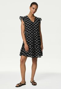 Abito nero con scollo a V, maniche a cappuccio e motivo geometrico bianco. Realizzato in tessuto leggero, presenta una silhouette svasata e un orlo fino al ginocchio.