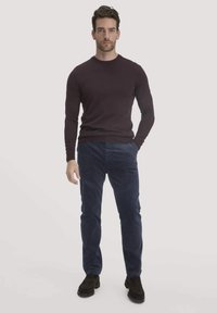 Dunkelvioletter Rundhalsausschnitt-Pullover, figurbetont, kombiniert mit navycordfarbener Cordhose. Das Modell trägt schwarze Wildlederschuhe. Einfaches, modernes Design mit strukturierten Stoffen.