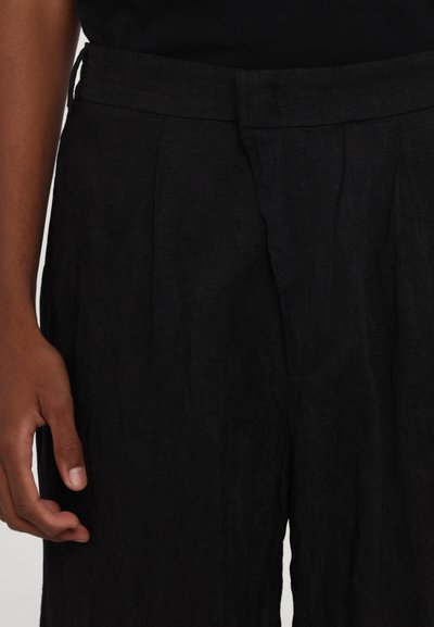 Pantalones de lino negros con una superficie texturizada, que presentan un corte ajustado, pliegues en la parte delantera y una cinturilla con trabillas para cinturón.