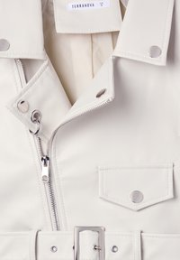 Giacca in ecopelle bianca con chiusura a cerniera, bottoni a pressione e vita con cintura. Include dettagli in metallo argentato e tasca applicata.