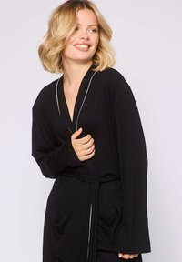 Schwarzer Kimono-Robenstil mit strukturiertem Stoff, langen Ärmeln, seitlichen Taschen und weißen Besätzen entlang des Kragens und der Manschetten.