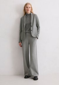 Costume gris côtelé comprenant un blazer cintré à deux boutons et un pantalon à jambes larges. Le tissu présente une texture douce, complétée par un haut à col montant.