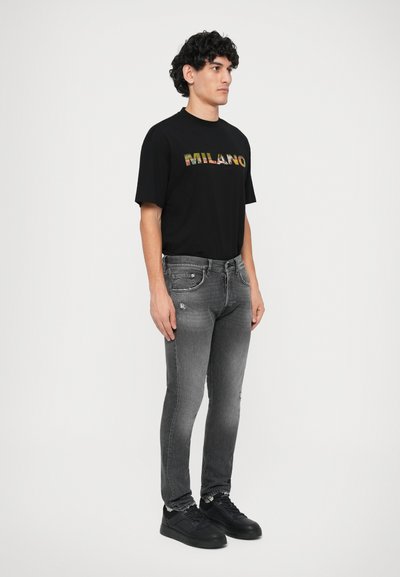 Svart t-shirt med "MILANO" i flerfärgad text, kombinerad med åtsittande grå jeans med slitna detaljer och svarta sneakers.