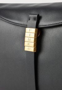 Black leather bag with a gold clasp featuring vertically stacked letters spelling "PINKO" on the front flap.