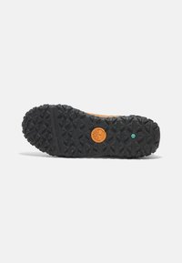 Suela de goma con tacos profundos para tracción, con un logo naranja y un acento verde. Color negro con patrones texturizados para mejor agarre.