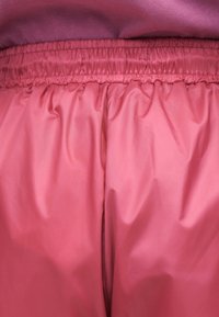 Gros plan de la ceinture élastique sur un pantalon rose brillant avec un tissu rose visible au-dessus de la ceinture.