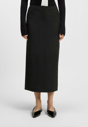 Black high-waisted pencil skirt made of a smooth fabric; features minimal seams and a slit pocket, paired with black pointed-toe shoes.
