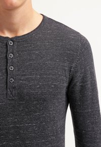 Tmavě šedé tričko henley vyrobené z měkké tkaniny, s kulatým výstřihem, čtyřmístným odhalením na knoflíky a jemným strukturovaným vzorem.