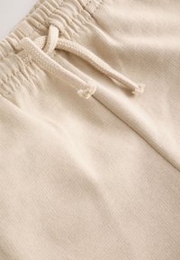 Gros plan sur un tissu beige avec une taille élastique et deux cordons tressés assortis noués en boucle.