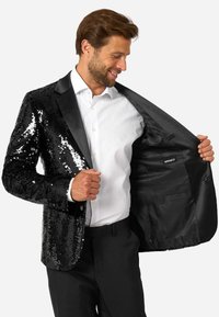 Blazer nero con paillettes e rever in satin, taglio slim, che mostra una camicia bianca sottostante. Interno foderato in tessuto nero con dettagli della tasca.
