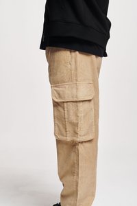 Beige corduroy cargobroek met verticale ribbels. Voorzien van grote zijzakken en een relaxte pasvorm, gecombineerd met een zwarte hoodie.