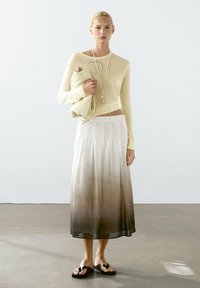 Ljusbeige tröja, flödande vit kjol med en ombré-effekt från vitt till brunt, och svarta flip-flops. Modellen håller en ljus väska.