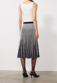 Jupe midi rayée noir et blanc, texture plissée, taille élastique, associée à un haut sans manches blanc et des talons hauts noirs.