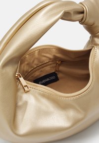 Guldfarvet håndtaske i imiteret læder med en knudet hank, glat tekstur og en lynlåslomme indeni. Inderforet har et mærke.