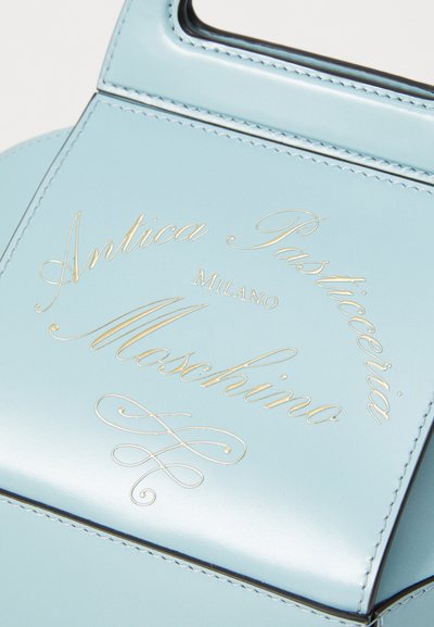 Geantă din piele de culoare albastru deschis, cu text embosat în aur care spune "Antica Pasticceria Milano Moschino", caracterizată prin cusături îngrijite și un design structurat.