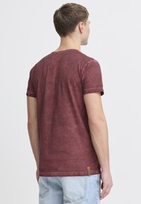 Bordeauxrot Kurzarm-T-Shirt mit weicher Textur und leicht verwittertem Aussehen, versehen mit einem kleinen Logostick auf dem unteren Saum.