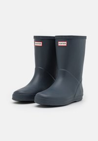 Une paire de bottes de pluie en caoutchouc noir Hunter avec des semelles texturées et des logos près du haut, sur un fond blanc uni.