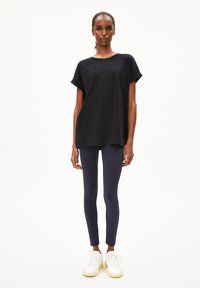 Maglietta nera in cotone con maniche corte, abbinata a leggings blu navy e sneaker bianche con suola testurizzata e punta arrotondata.