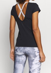 Černý atletický top s křížovým designem na zádech. Měkký, elastický materiál doplněný šedobílými legínami s batikovaným vzorem a proužkovaným motivem.