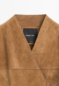 Vêtement en cuir suédé marron avec col visible et étiquette noire portant la mention "Massimo Dutti" cousue à l'intérieur.
