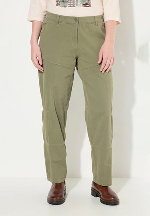 Pantalones verde claro con un corte relajado, detalles de costura visibles y dos bolsillos frontales, combinados con botas marrones hasta el tobillo.