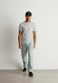 Grå t-shirt med et lille grafisk motiv, lyseblå jeans og sorte sneakers. Tilbehøret inkluderer en sort kasket. Enkel og afslappet outfit.