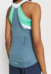 Top in blu e verde con schiena in rete, vestibilità slim e dettagli arricciati. Presenta un logo vicino all'orlo e diverse texture del tessuto.