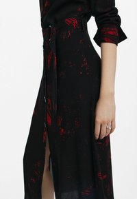 Mustmustel dress punase abstraktsete mustritega, pikad varrukad ja vöödiga talje. Omab külgsuleta ja nupuvajutust. Kerge kangas.