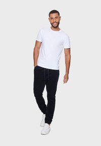 T-shirt blanc à col rond, pantalon de jogging bleu marine avec cordon de serrage et baskets blanches. Tissu lisse avec une coupe décontractée et un design de jambe fuselée.