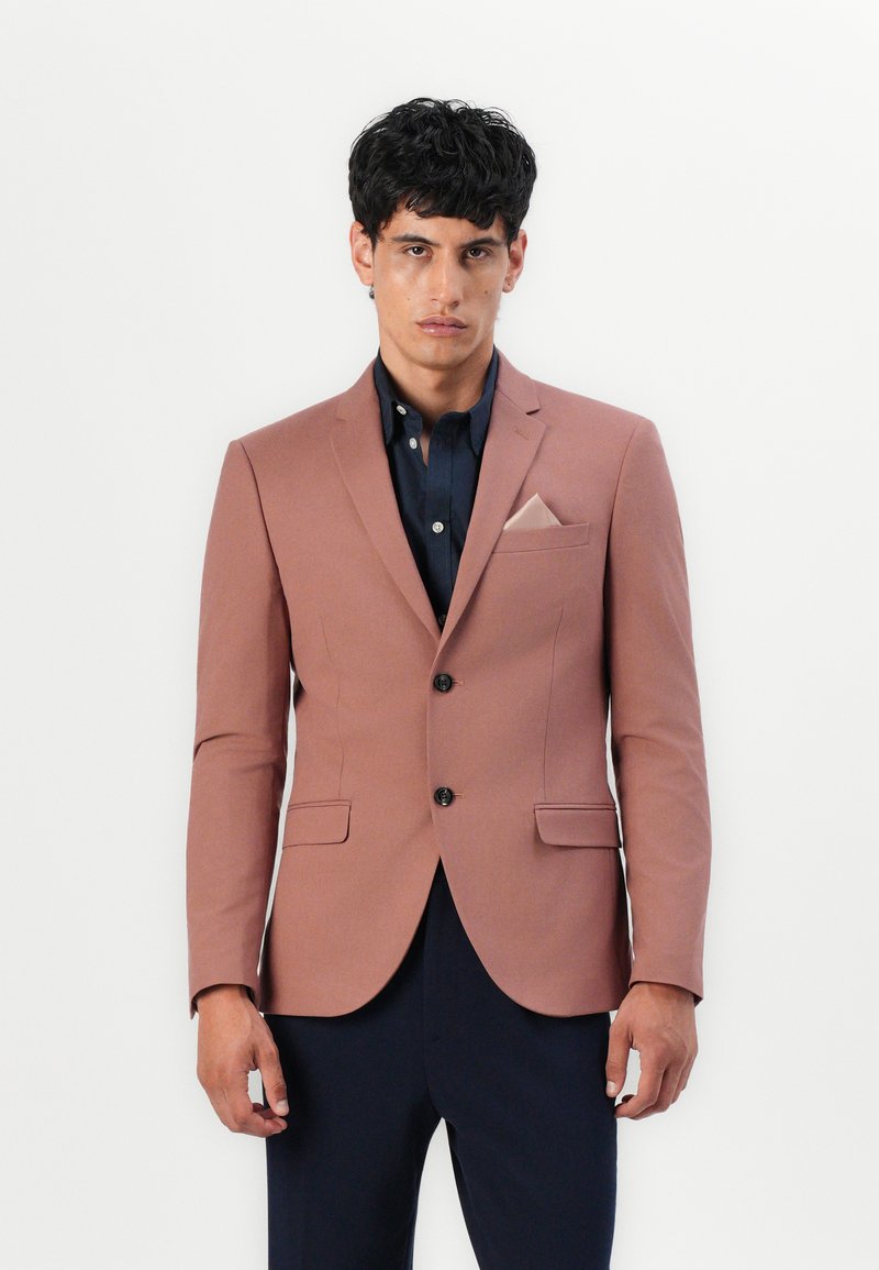 Ανοιχτό ροζ σακάκι με προσαρμοσμένη γραμμή, δύο μπροστινές τσέπες, κλείσιμο με μονή κουμπί και μπλε πουκάμισο από κάτω; διαθέτει μαντήλι τσέπης.