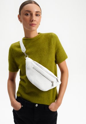 Marsupio in pelle bianca con finitura testurizzata, dotato di tasca frontale con zip e tracolla regolabile, indossato sopra un maglione verde.